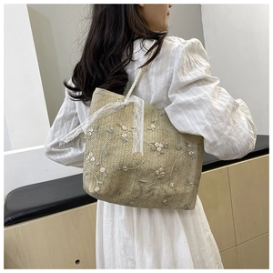 Detail of straw tote bag with floral embroidery and white lace ribbon decoration