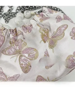 Detail of pink and gold butterfly jacquard fabric with silver chain and white pearl beads