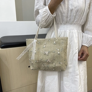 Beige woven handbag with floral embroidery and white lace ribbon, model shot