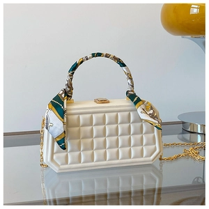 Close-up of white quilted box bag featuring a silk scarf handle and gold chain strap