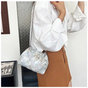 Detail of blue and gold butterfly embroidery on a white satin bucket bag with pearl handle