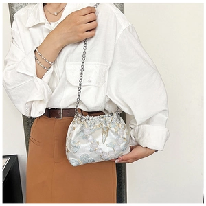Detail of white satin cloud bag featuring blue butterfly embroidery and pearl handle