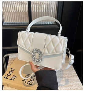 Detail of white quilted crossbody bag with sparkling rhinestone buckle and top handle