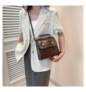 Detailed view of a dark brown retro crossbody bag worn by a model in a minimalist room