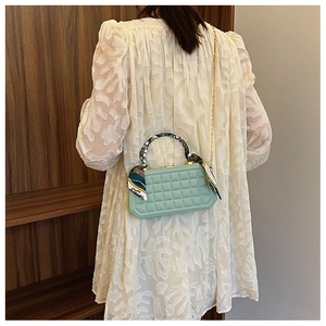 Detail of mint green quilted handbag with decorative silk scarf on handle and gold chain