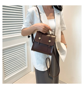 Detail of dark brown matte leather crossbody bag with round metal buckle on a model