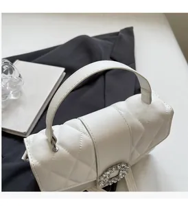 Detail of white quilted crossbody bag with a round crystal-encrusted decorative buckle