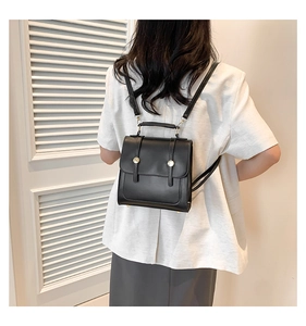 Detail of minimalist black faux leather backpack with gold buckle on a white blazer