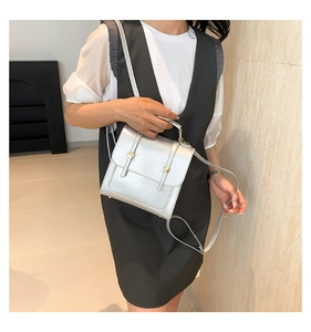 Detail view of a silver metallic rectangle crossbody bag with gold tone buckles on a model