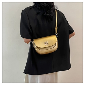Sac besace doré élégant avec boucle métallique porté sur une veste de tailleur noire