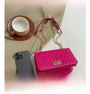 Sac bandoulière matelassé rose vif avec chaîne dorée à côté d'un smartphone