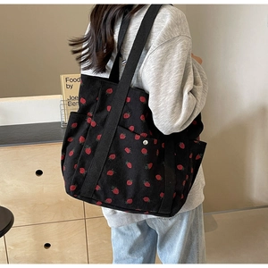 Détail du sac cabas en velours côtelé noir avec broderie fraise et poches pratiques