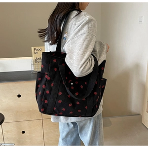 Vue latérale d'un grand sac cabas en velours côtelé noir avec imprimé fraise porté