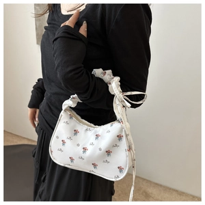 Close-up of a white floral baguette bag with a ruched cloud strap and bow detail