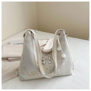 Detail of white silk tote bag with floral embroidery and silver bow pendant