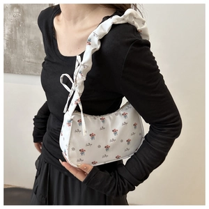 Detail view of white underarm bag with dense floral print and wide shoulder strap