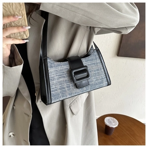 Détail d'un sac porté épaule en denim avec finitions cuir noir sur un mannequin en tailleur