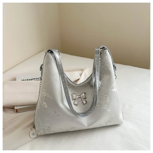 Close-up of white satin tote bag featuring floral embroidery and a silver metal bow accent