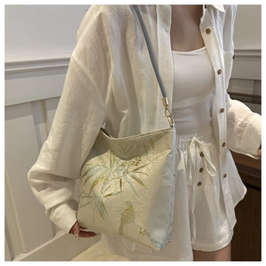 Detail view of bird and bamboo leaf embroidery on a cream textured shoulder bag