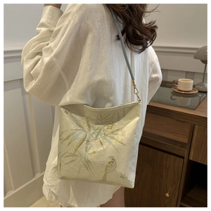 Detail of embroidered bamboo leaves and bird on a cream shoulder bag shown on model