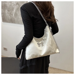Detail of cream tote with silk embroidery, silver bow, and pearl charm on a model