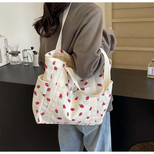 Detail of white corduroy tote bag featuring red strawberry print and wide shoulder strap