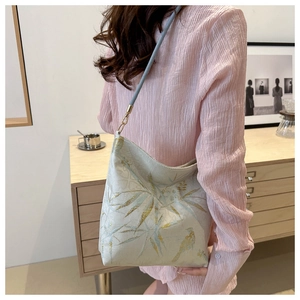 Detail of bamboo and bird embroidery on a cream single shoulder bucket bag with gold hardware