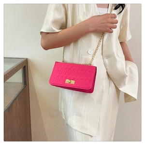 Détail d'un sac bandoulière matelassé fuchsia avec chaîne dorée et fermoir pivotant