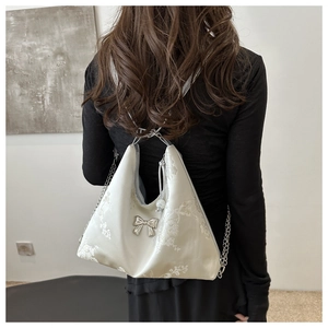 Detail of floral embroidery on satin hobo bag with a silver bow and metal chain