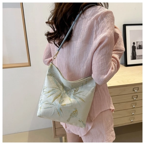 Detailed golden bamboo leaf and bird embroidery on elegant light-colored fabric shoulder bag