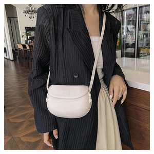 Minimalist beige saddle bag worn by a model in a café for everyday elegant outfit