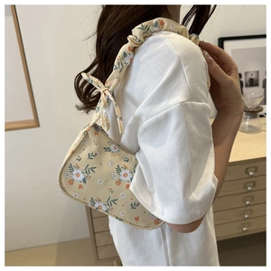 Detail of floral underarm bag showing beige fabric, flower patterns, and ruffled bow strap