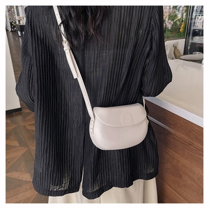 Minimalist beige saddle bag with adjustable strap worn over a black pleated top for women