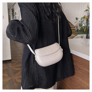 Side view of cream saddle crossbody bag on a model wearing a black pleated top