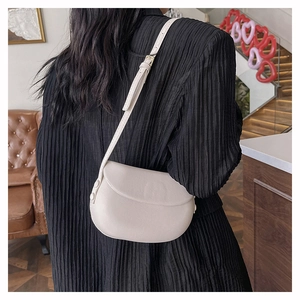 Lifestyle shot of a minimalist cream half-moon crossbody bag with an adjustable strap