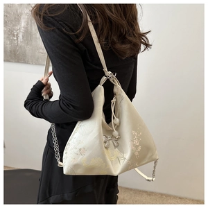 Detail of cream tote bag with floral embroidery, silver chain strap, and bow charm