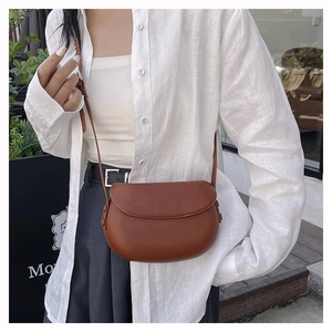 Detailed view of a brown leather saddle bag styled as a crossbody on a female model