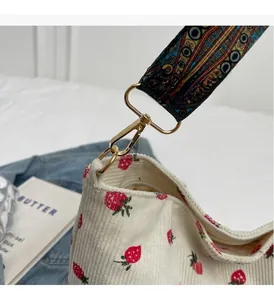 Close-up of strawberry corduroy bag with vintage floral strap and gold metal hardware