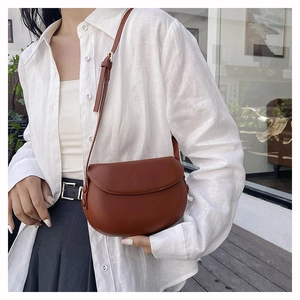 Detailed view of a vintage brown leather saddle bag styled on a white linen shirt model