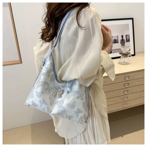 Close-up of a white shoulder bag with blue butterfly embroidery on a female model