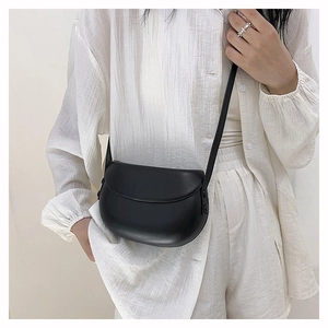 Minimalist black matte leather saddle bag shown on model with white pleated shirt