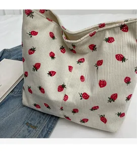Detail of strawberry print corduroy shoulder bag next to denim and a lifestyle book