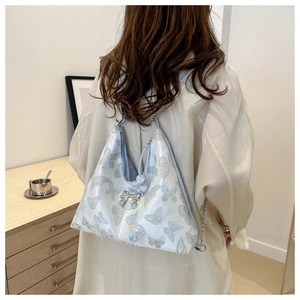 Detail of light blue butterfly print hobo bag with a silver bow charm on a satin surface