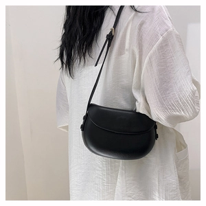 Side view of a minimalist black leather saddle bag with adjustable strap on a model