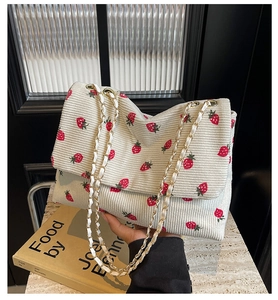 Close-up of cream corduroy shoulder bag featuring red strawberry prints and gold chain strap