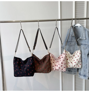 Detail view of strawberry print corduroy shoulder bags in four colors on a rack