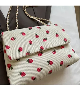 Macro shot of corduroy floral bag texture with red strawberry prints and gold woven chain