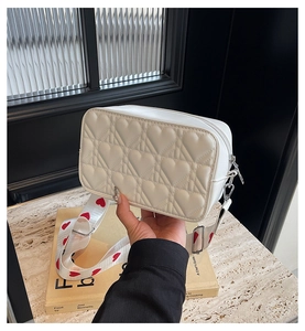 Close-up of white leather camera bag with heart quilting and red patterned wide strap