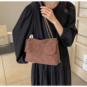 Detail of strawberry print on brown corduroy flap bag with gold chain shoulder strap