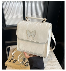 Detail of white handbag with textured pleats and a silver butterfly buckle on a stone surface